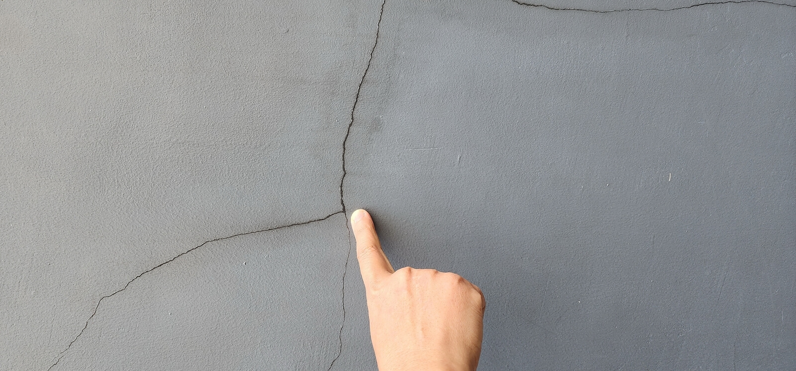 A hand pointing at crack in a wall | Buying a house with a basement